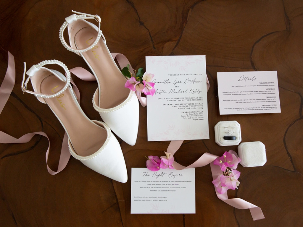 Wedding invitation suite, rings, and bridal shoes arranged on a wood table